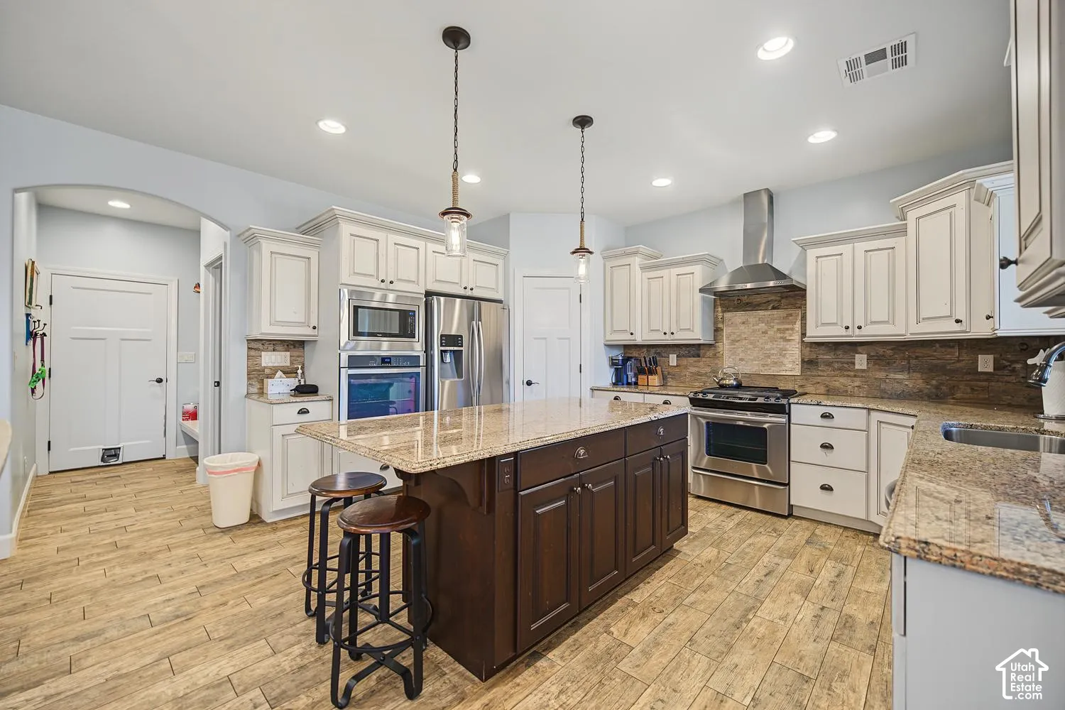 Kitchen featuring a central island with a contrasting dark finish, stainless steel appliances, stone-surface countertops, stone-tile backsplash, and wood-finish flooring
