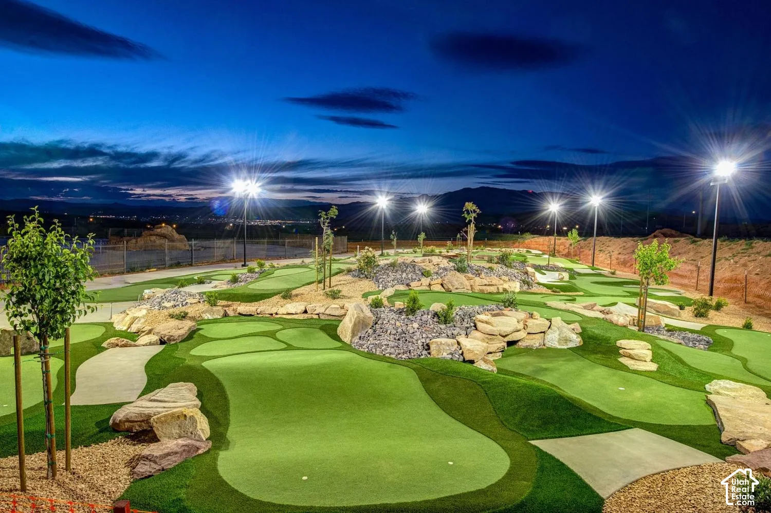 Custom synthetic turf putting green featuring integrated stone boulders, decorative rock landscaping, and pole-mounted lighting
