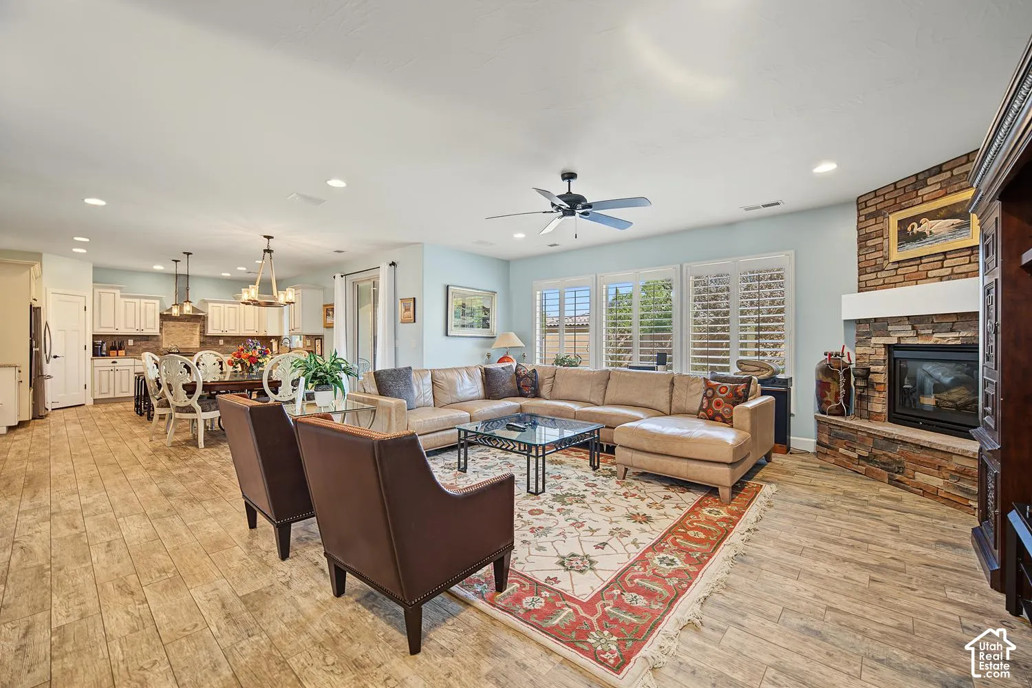 Open-concept space featuring wood-finish flooring, recessed lighting, a stone-accented fireplace, and plantation shutters