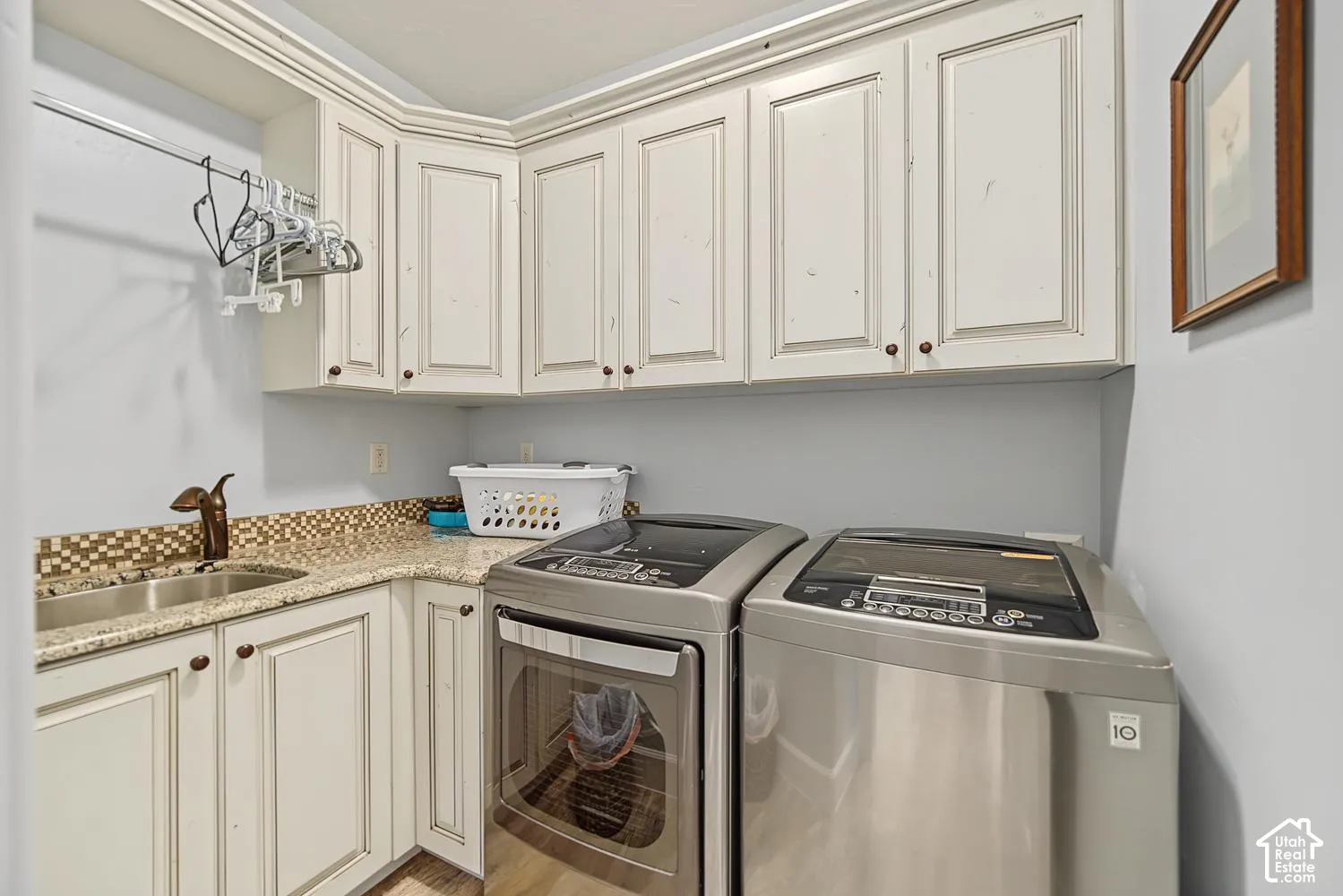 Laundry area featuring white cabinetry with raised-panel doors, stone-finish countertops, an integrated drop-in sink, and a decorative tile backsplash