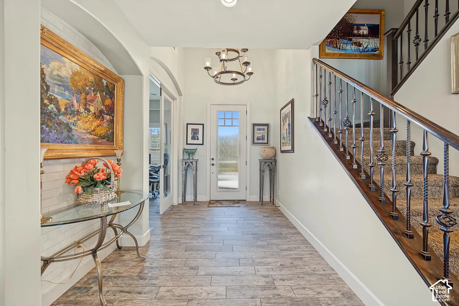 Foyer featuring wood-finish tile flooring, a multi-tiered circular chandelier, a staircase with decorative metal balusters and a wood handrail, and an arched entryway with French doors