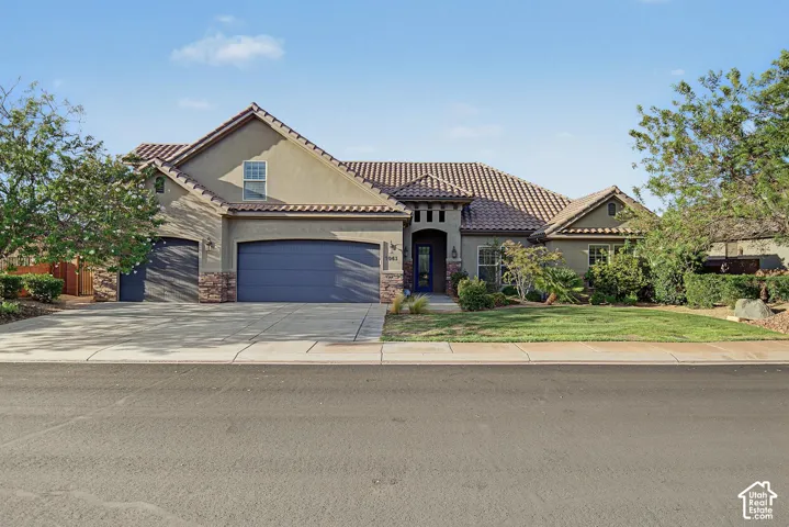 Single-story exterior featuring a clay tile roof, stone masonry accents, a three-car garage, and a manicured front lawn