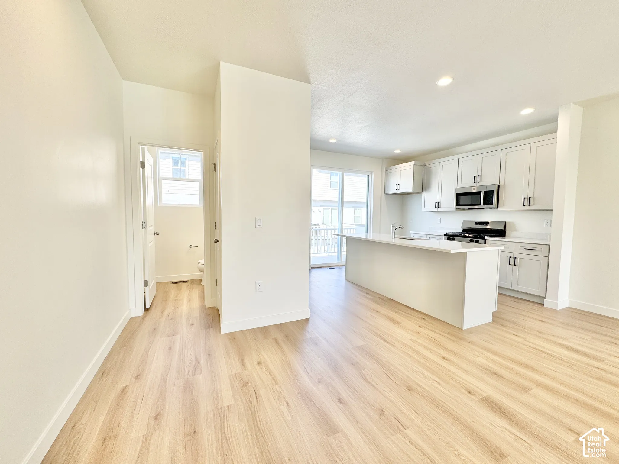 Kitchen featuring white shaker-style cabinetry, quartz countertops, a central island with an integrated sink, recessed lighting, and wood-finish flooring