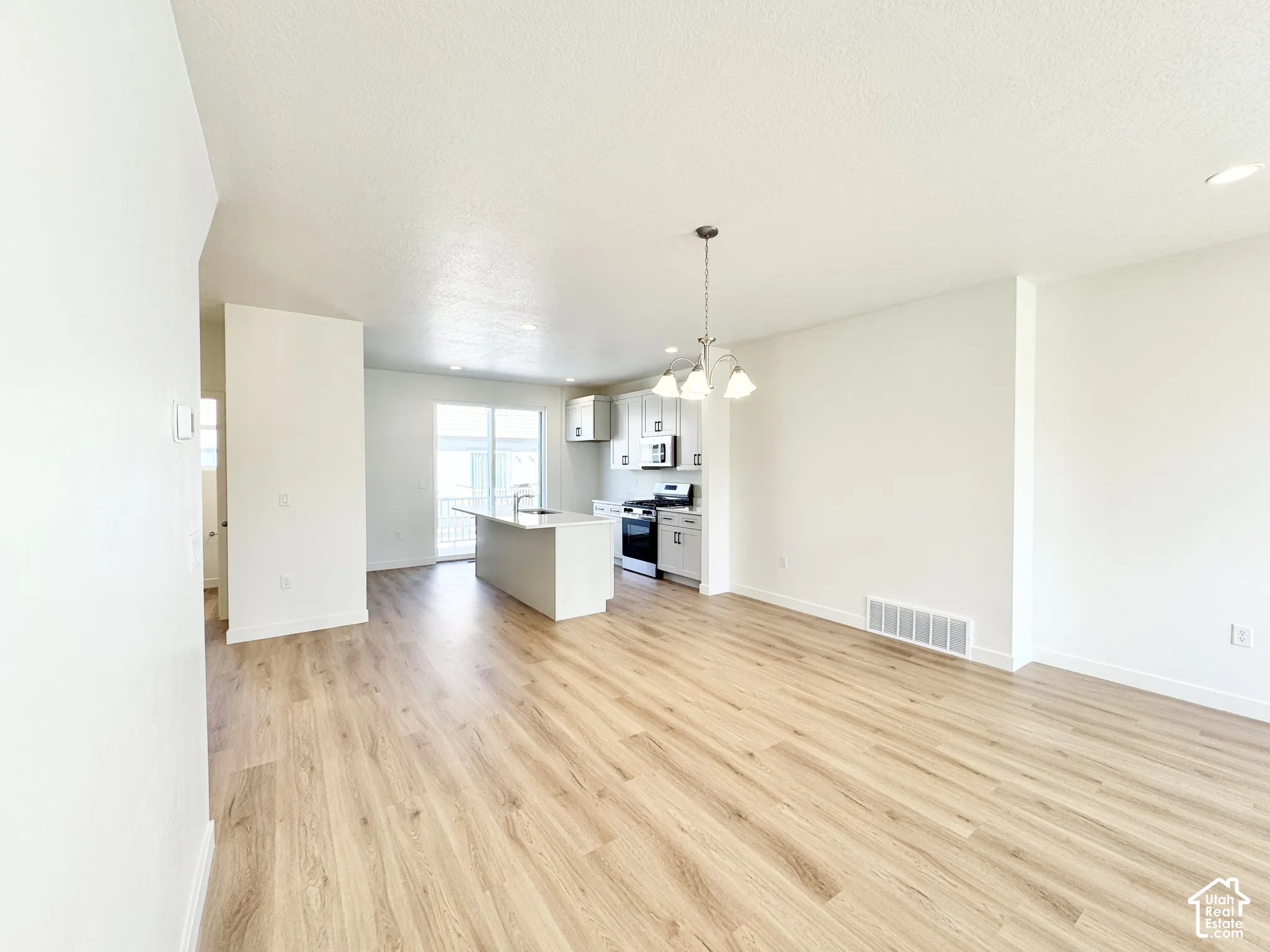 Open-concept area featuring wood-finish flooring, a kitchen island, white cabinetry, recessed lighting, and a multi-light pendant fixture