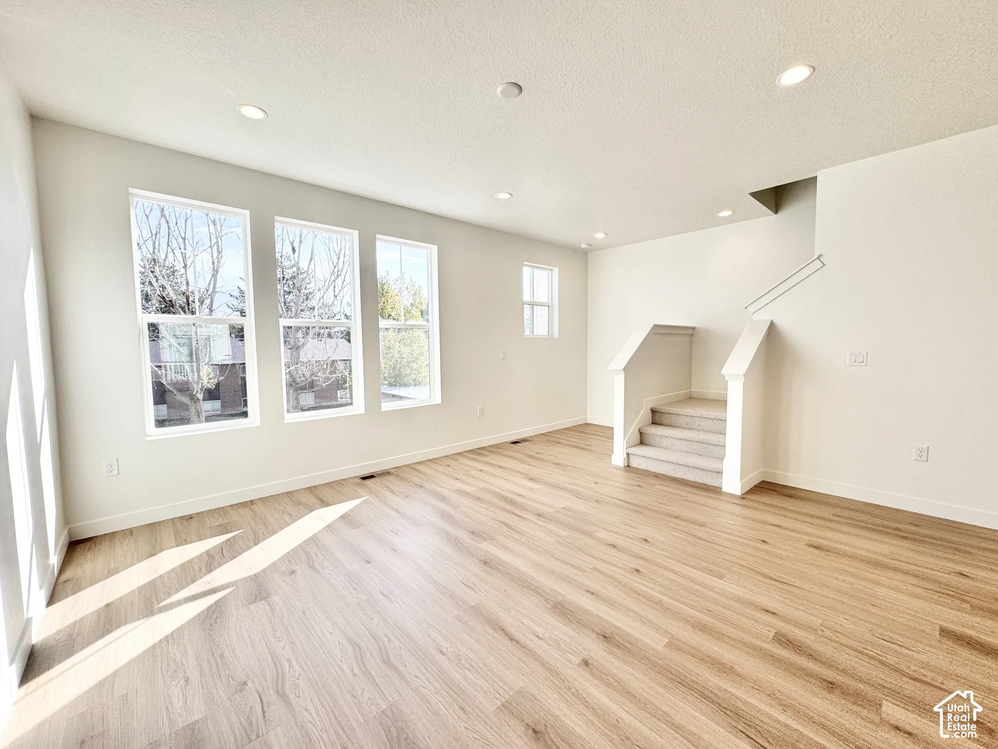 Interior space featuring light-toned wood-finish flooring, recessed lighting, multiple multi-pane windows, and a staircase with neutral carpeting