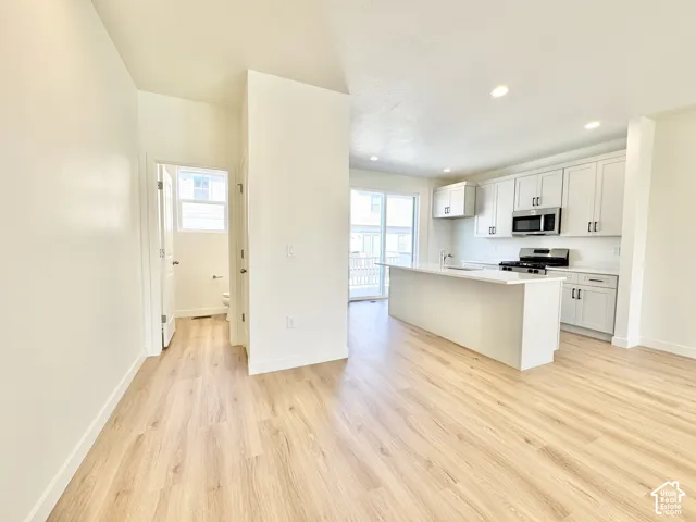 Kitchen featuring white shaker-style cabinetry, quartz countertops, a central island with an integrated sink, recessed lighting, and wood-finish flooring
