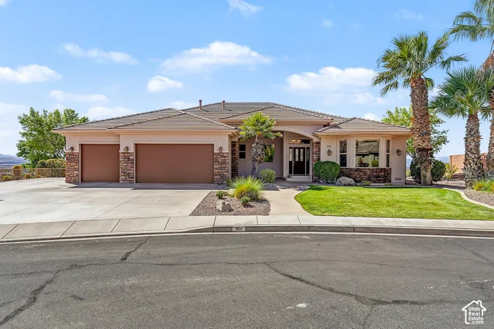 Single-level exterior featuring a stucco facade, stone veneer accents, multi-car garage, concrete driveway, and professional landscaping