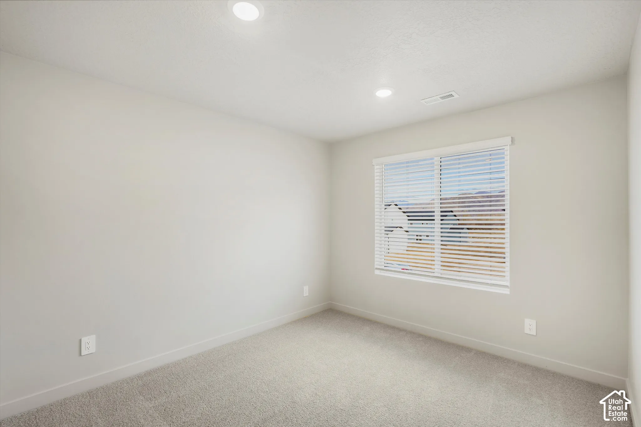 Neutral-toned room featuring high-pile wall-to-wall carpeting, recessed ceiling lighting, and a single window with horizontal blinds