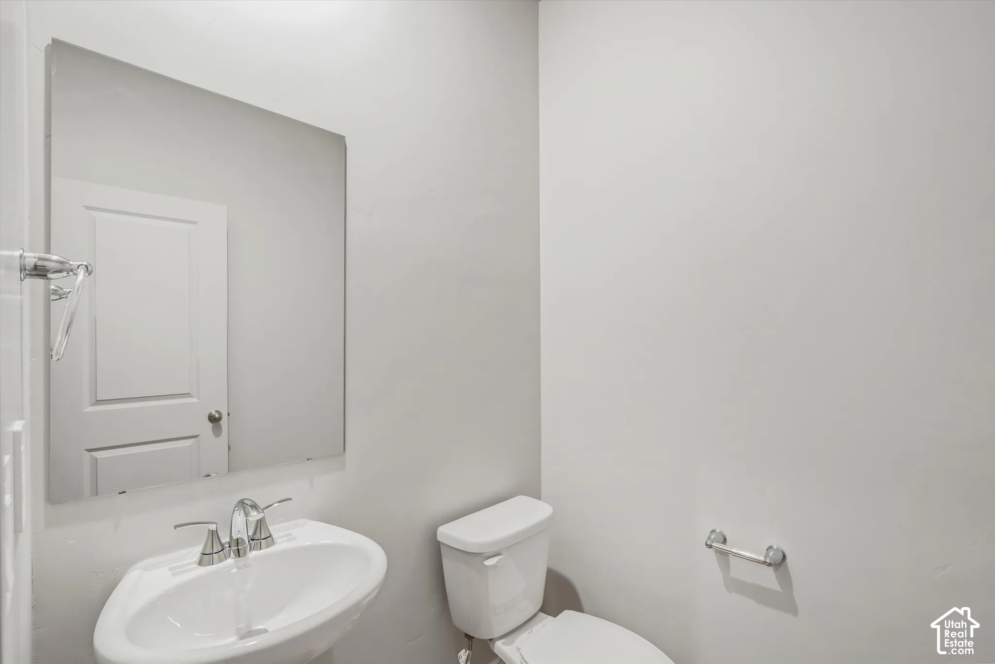 Wall-mounted rectangular mirror, pedestal sink with chrome dual-handle faucet, and white porcelain toilet