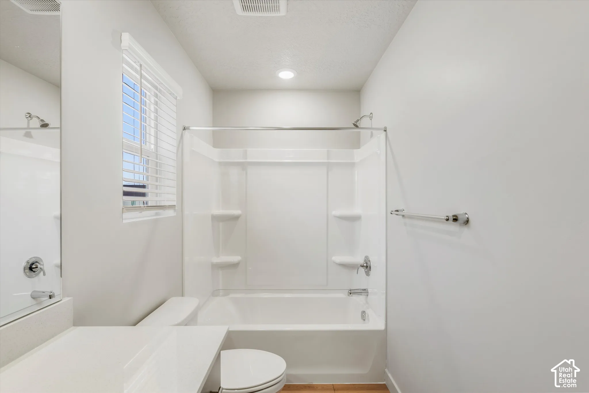 Full-size bathtub with integrated shelving, chrome shower fixtures, white vanity countertop, recessed lighting, and wall-mounted towel bar