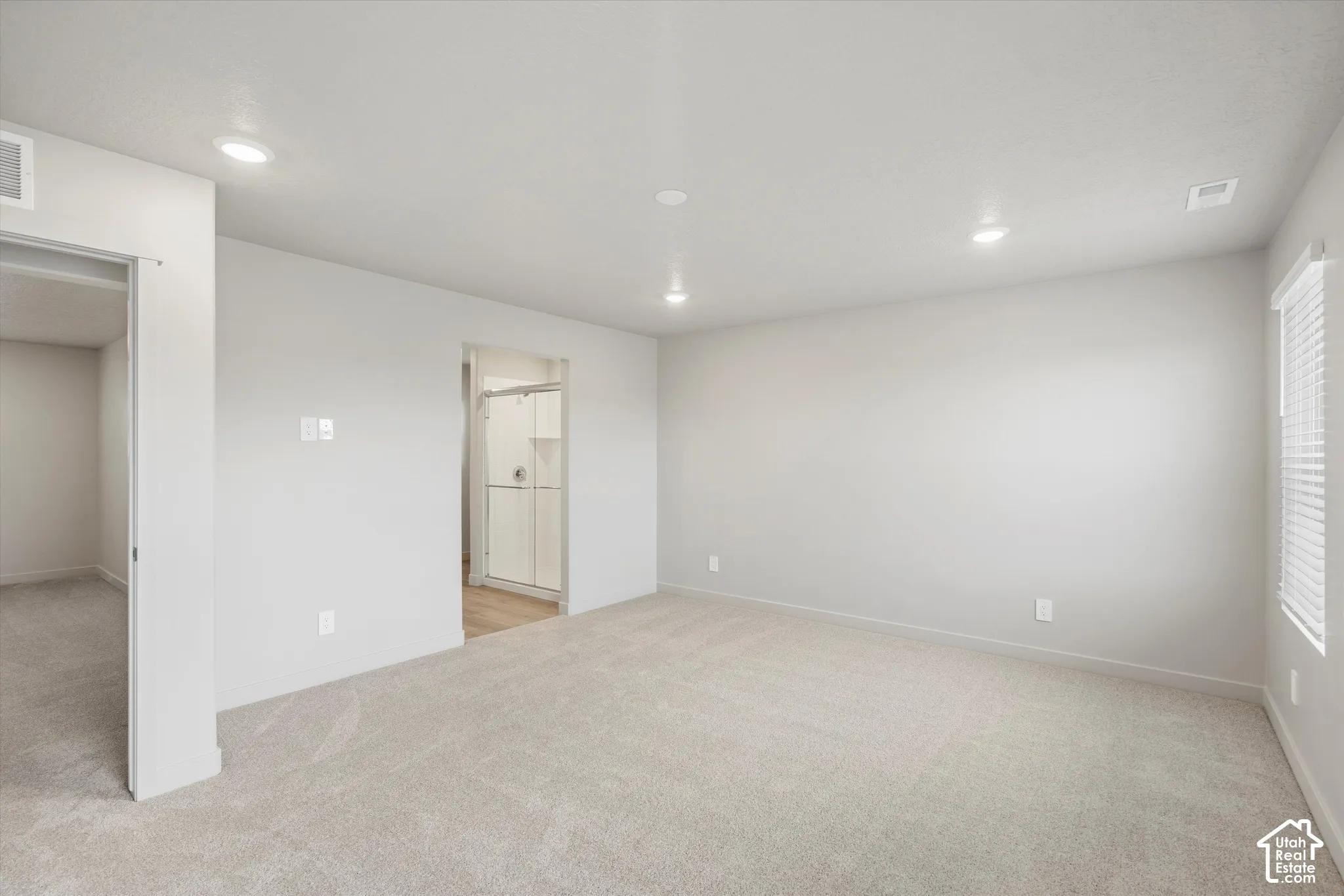 Neutral-toned interior space featuring wall-to-wall carpeting, recessed ceiling lighting, and horizontal blinds