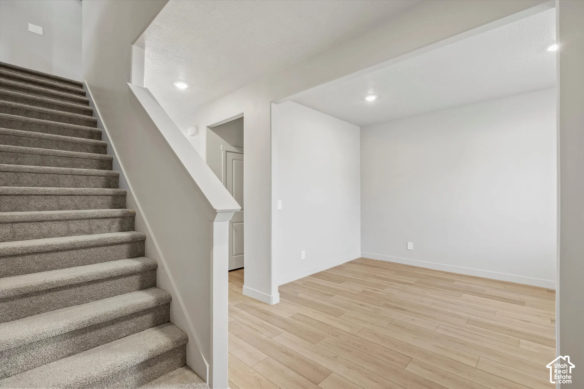 Staircase with neutral carpeting and a painted railing, complemented by wood-finish flooring and recessed ceiling lighting