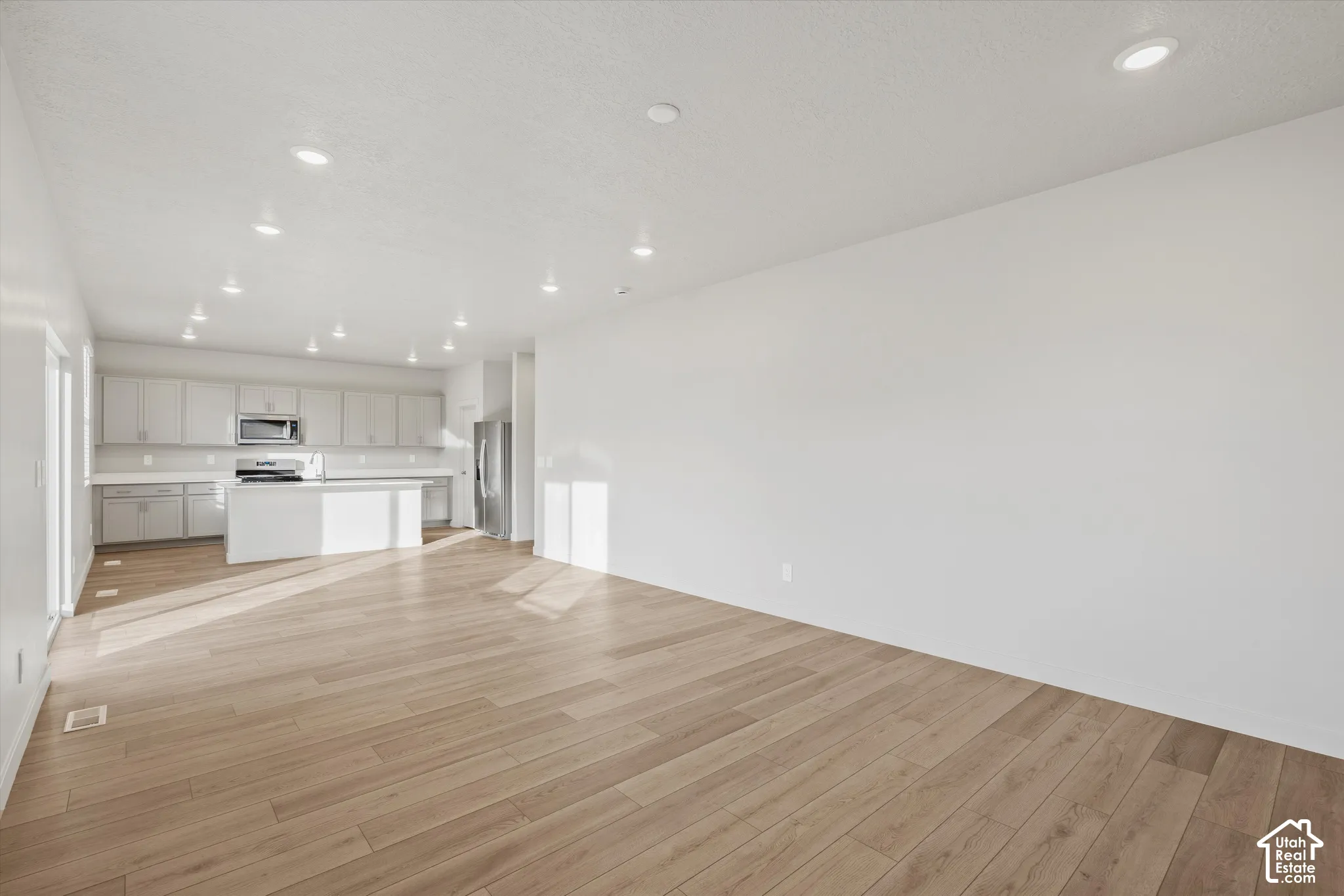 Open-concept interior featuring wood-finish flooring, recessed lighting, a central kitchen island, and neutral-toned cabinetry