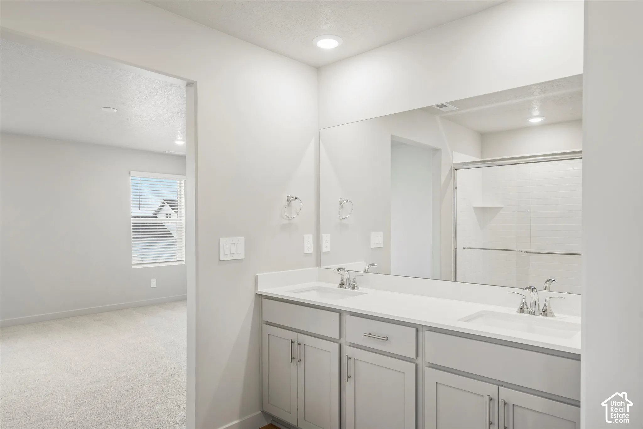 Dual-vanity cabinetry with rectangular under-mount sinks, solid-surface countertop, full-width wall mirror, and shower enclosure with sliding glass door
