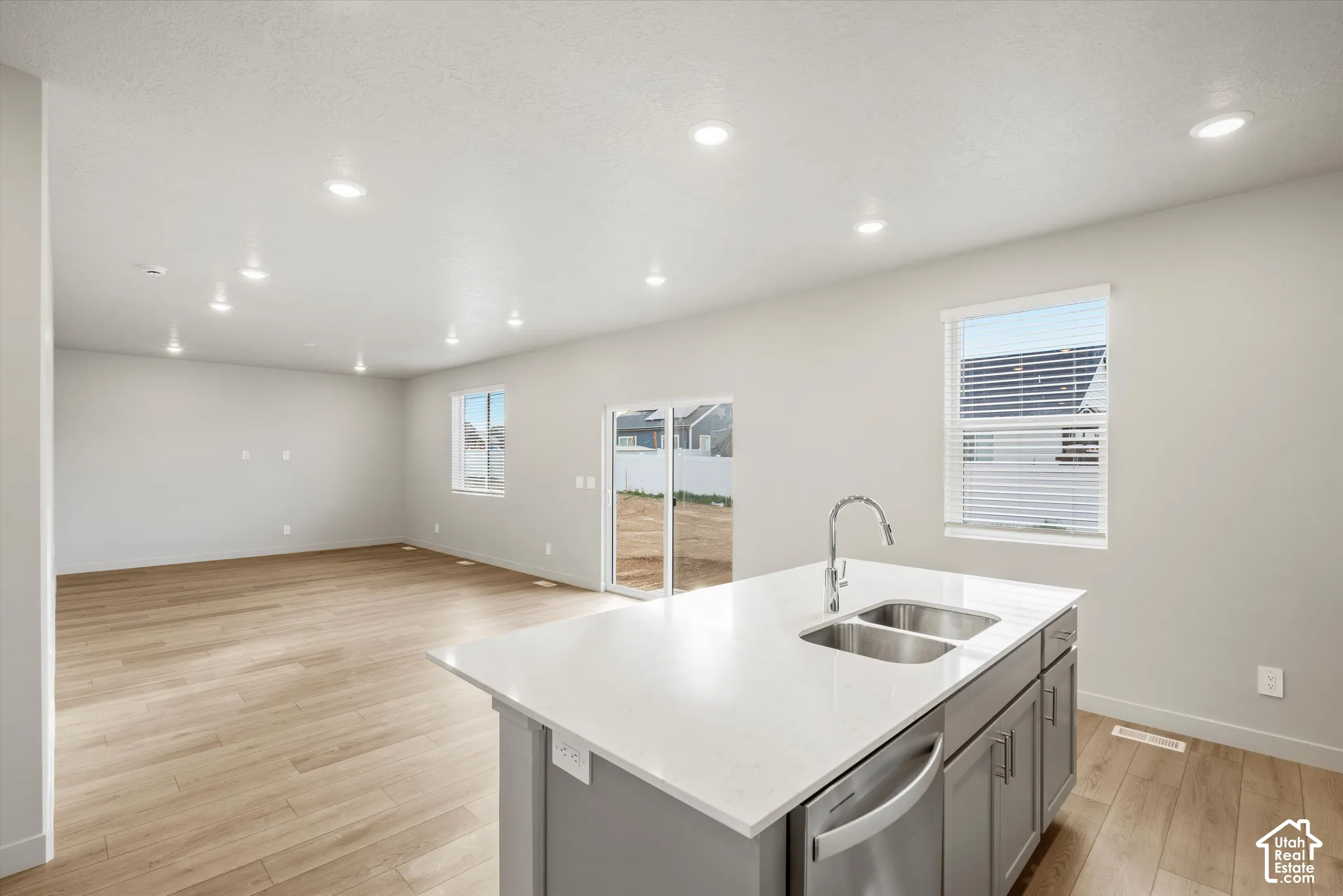 Kitchen island with white composite countertop, dual-basin stainless steel sink, recessed ceiling lighting, and wood-finish flooring