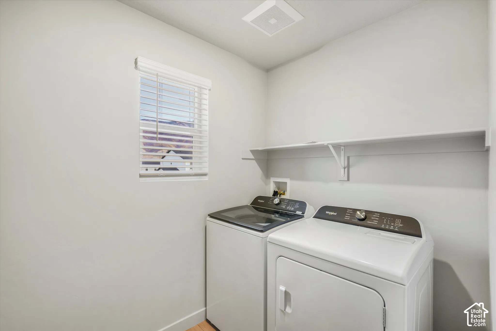Laundry area featuring a window with horizontal blinds, neutral wall paint, and a built-in wall-mounted shelf
