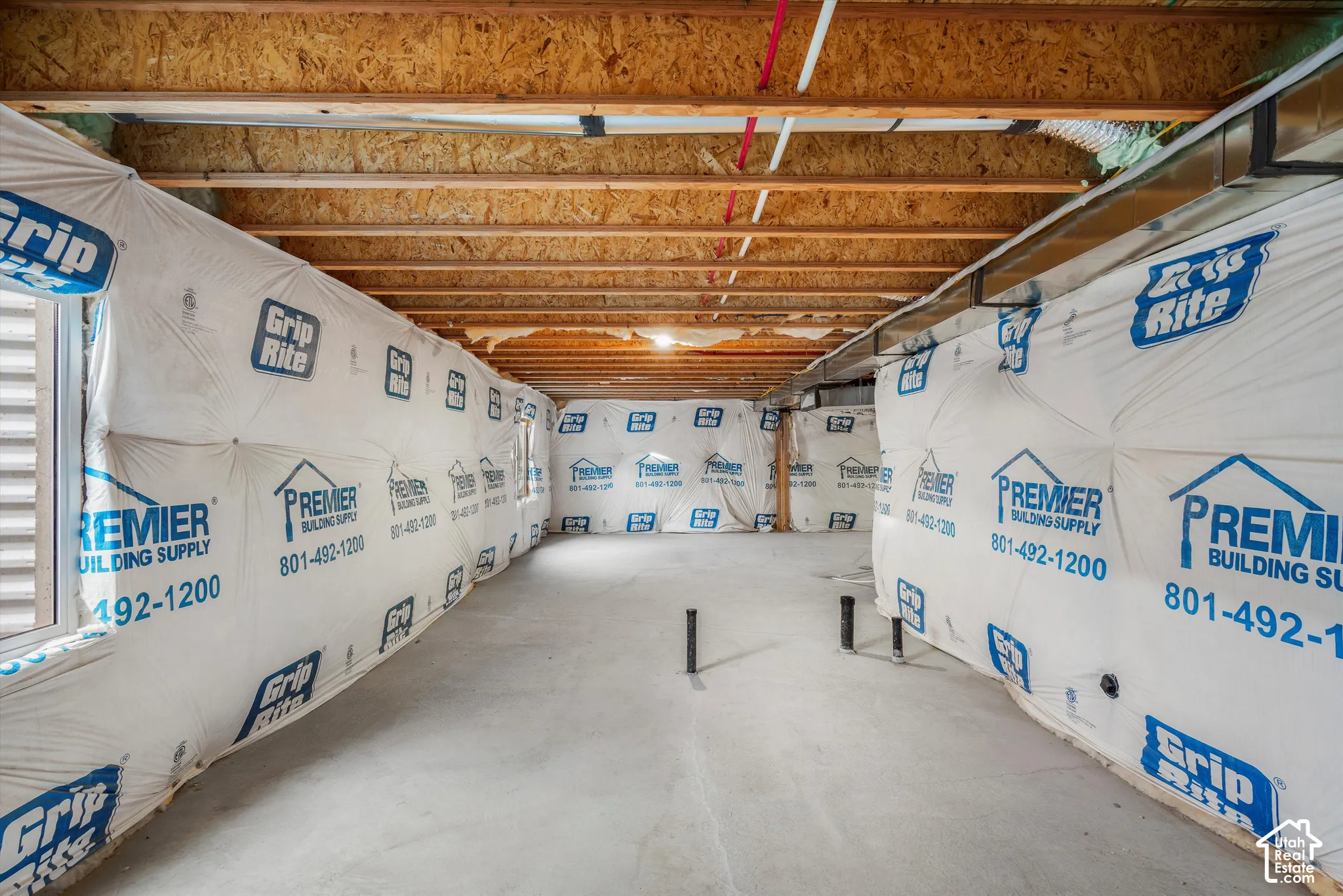 Unfinished space featuring exposed wood joists, concrete flooring, vapor barrier wall insulation, and capped plumbing stubs