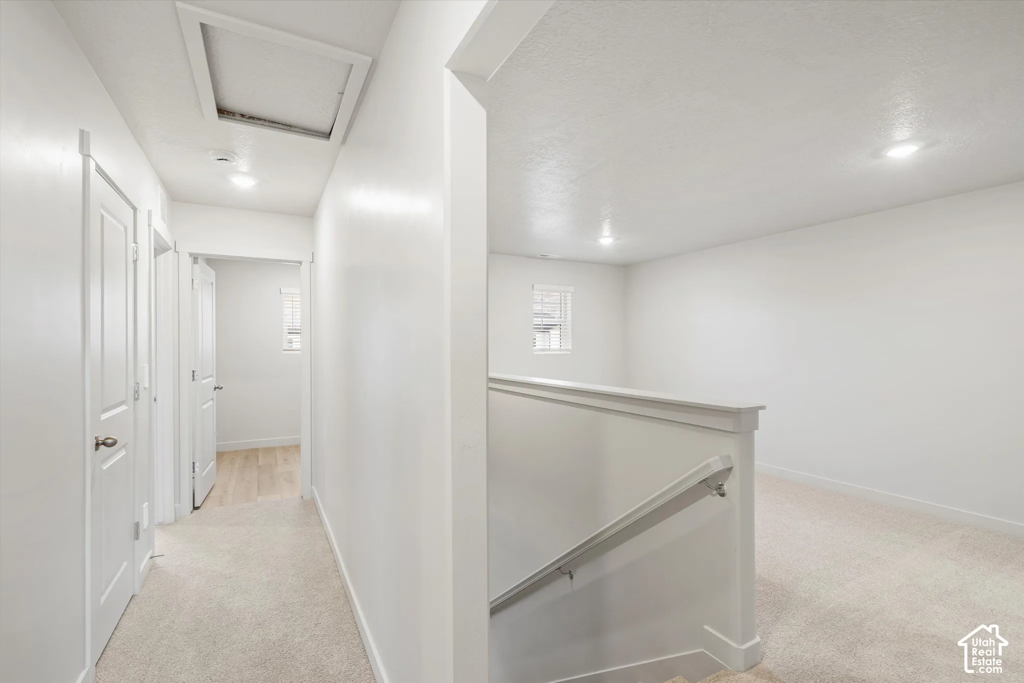 Hallway featuring neutral carpet, recessed lighting, white interior doors, and a staircase with a white handrail