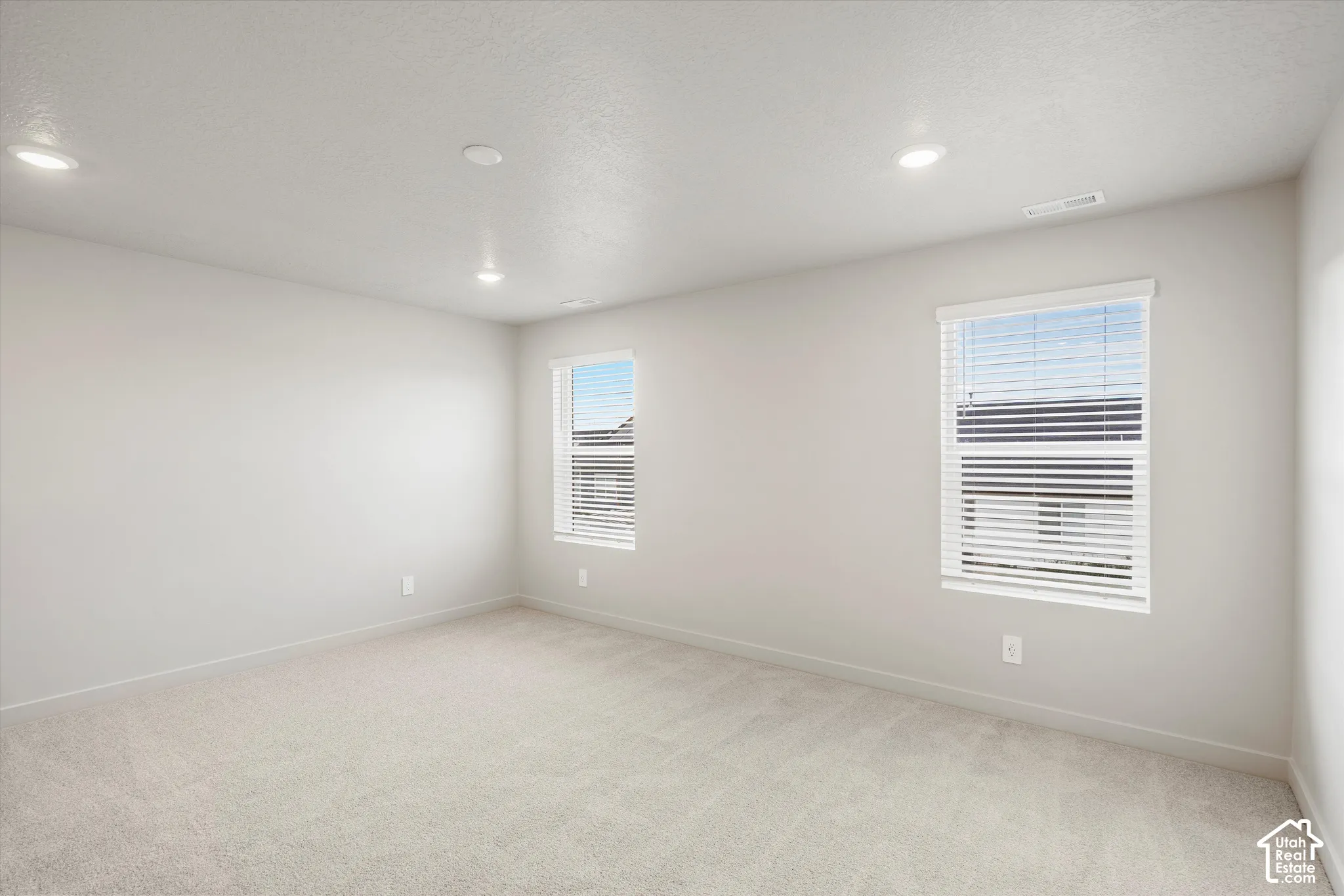 Neutral-toned interior space featuring neutral wall-to-wall carpeting, recessed ceiling lighting, and dual windows equipped with horizontal blinds