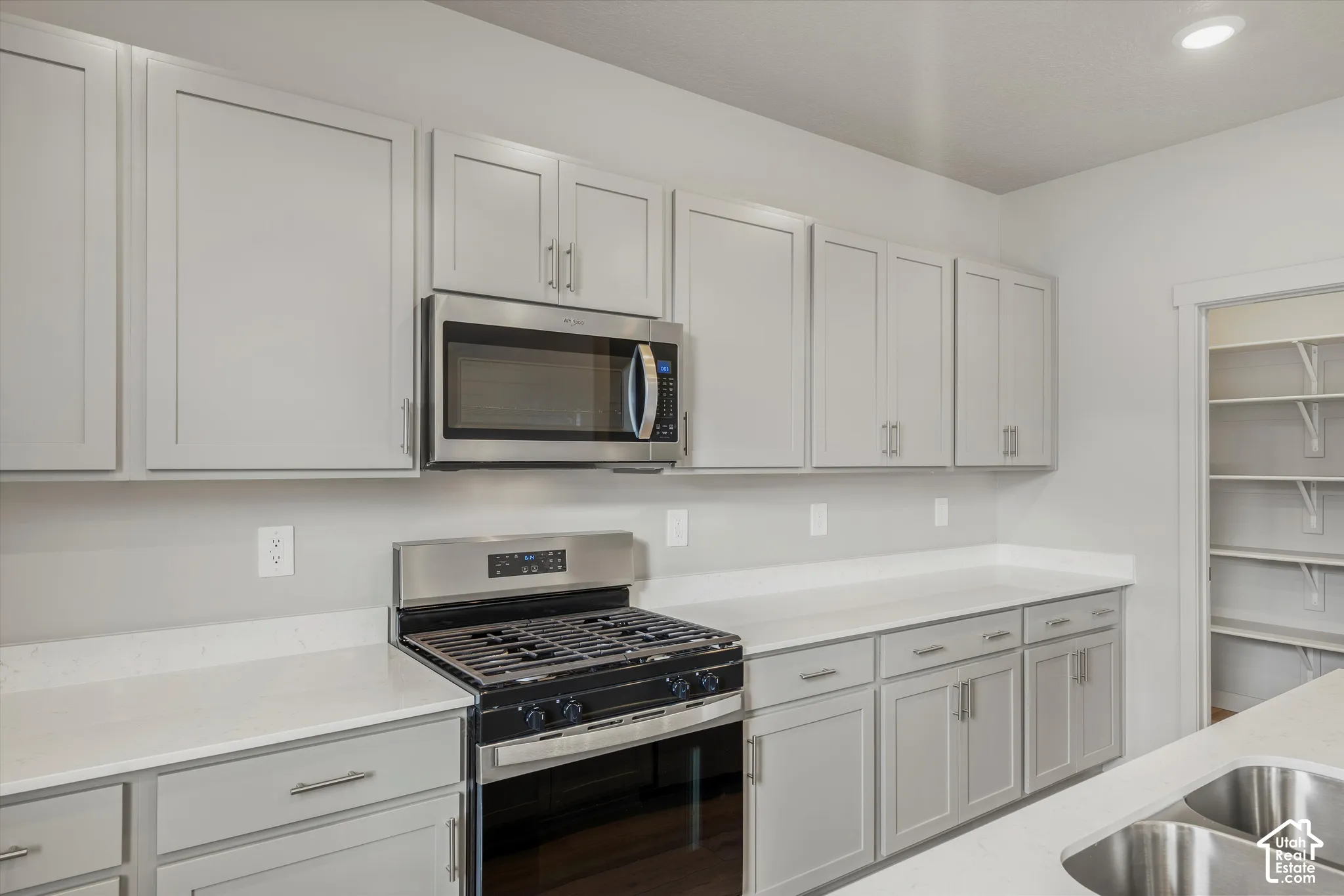 Kitchen featuring grey shaker-style cabinetry, quartz countertops, stainless steel gas range, built-in microwave, and an integrated pantry with tiered shelving