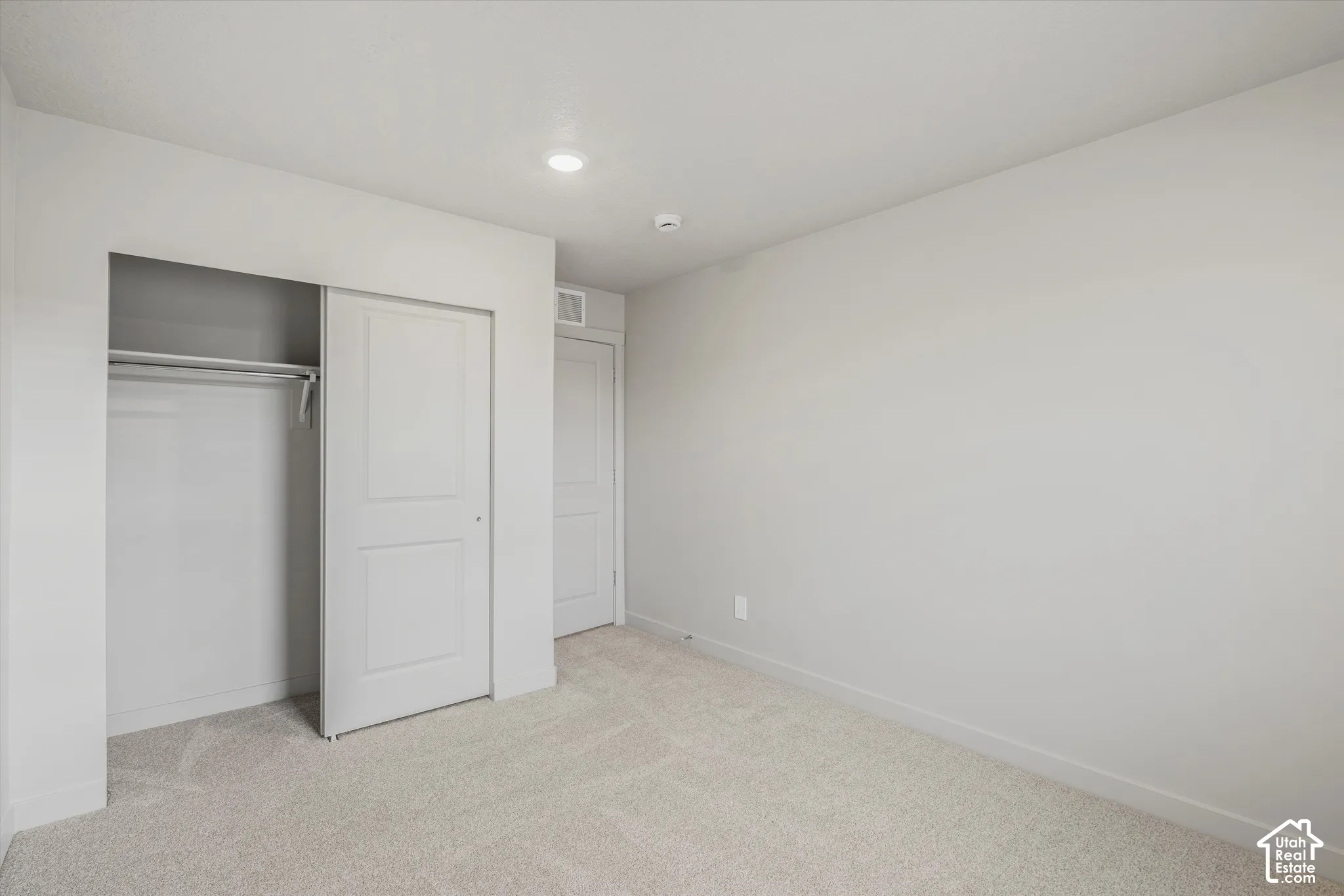 Neutral-toned interior space featuring light-colored wall-to-wall carpeting, recessed ceiling lighting, a built-in closet with sliding panel doors, and two interior doors with molded detailing
