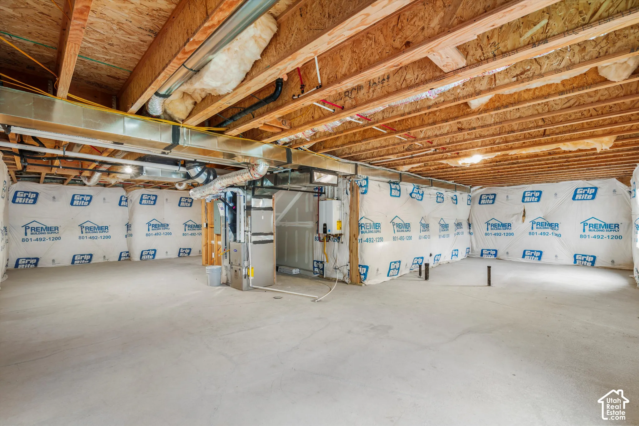 Unfinished lower level featuring concrete flooring, foundation wall vapor barriers, exposed ceiling joists, an installed furnace, and a tankless water heater