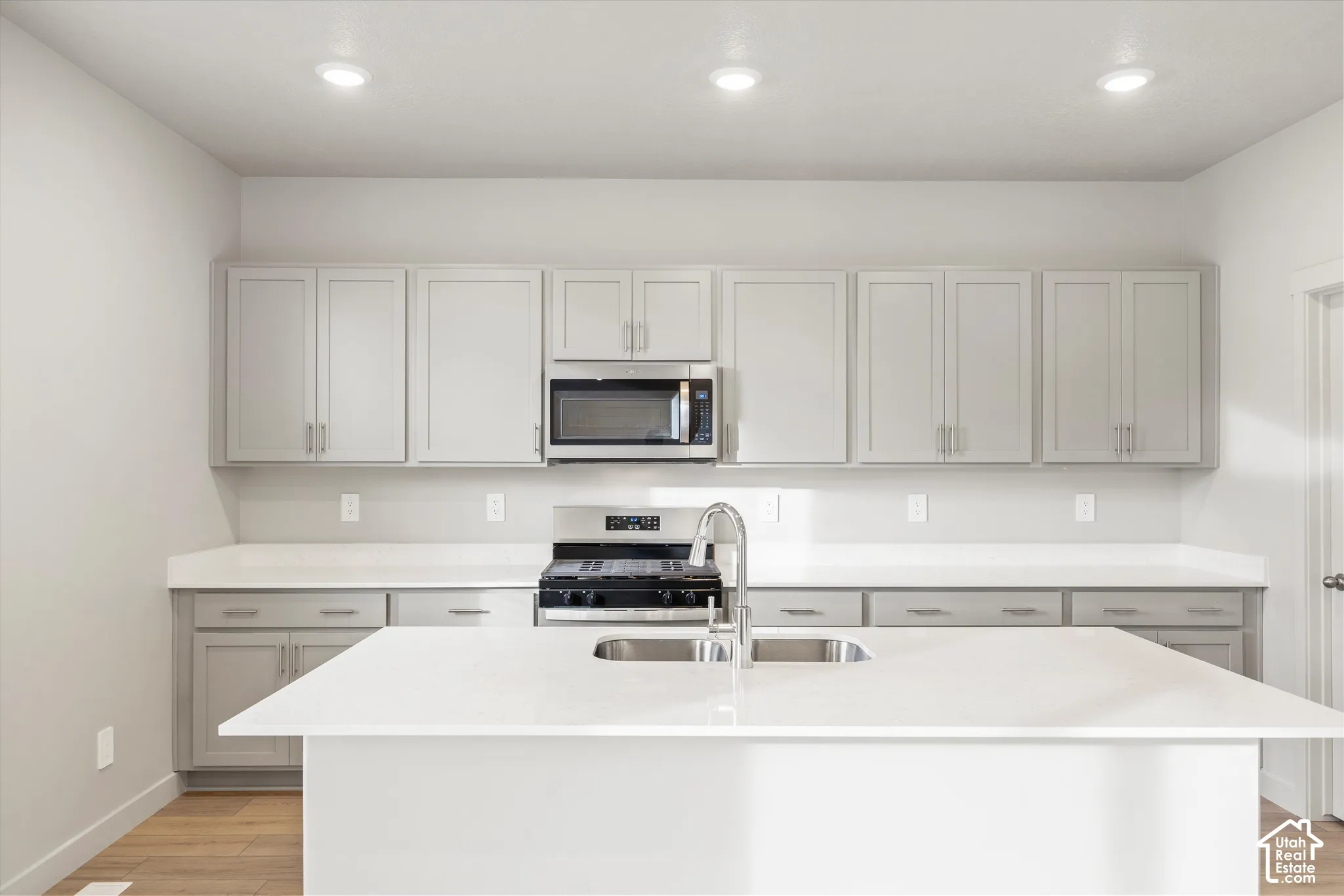 Kitchen featuring light gray cabinetry, solid-surface countertops, central island with stainless steel double-basin sink, and recessed lighting