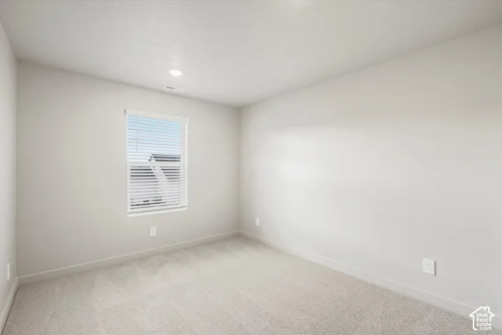 Neutral-toned interior space featuring wall-to-wall carpeting, light-colored wall finish, and a window with horizontal blinds