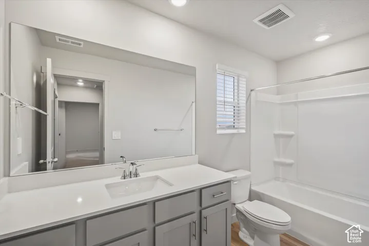 Bathroom featuring a vanity with a white countertop and integrated sink, full-width mirror, recessed lighting, and a white tub and shower combination with integrated shelving