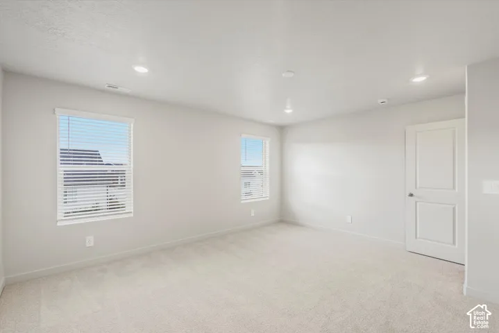 Neutral-toned interior featuring wall-to-wall carpeting, recessed ceiling lighting, and two windows equipped with horizontal blinds