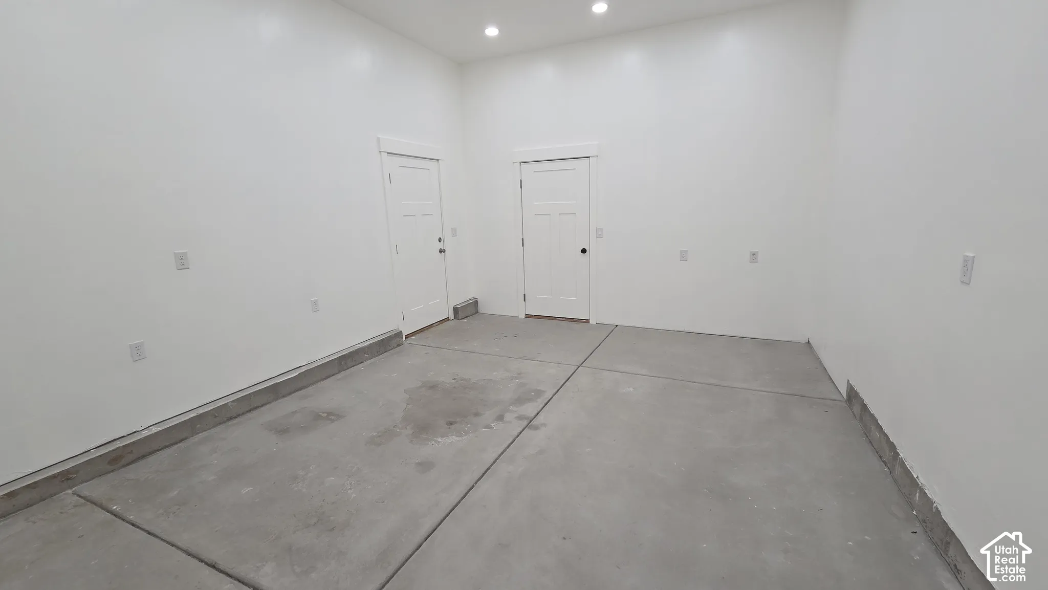 Finished garage interior featuring smooth white walls, high ceilings with recessed lighting, and two solid-core panel doors