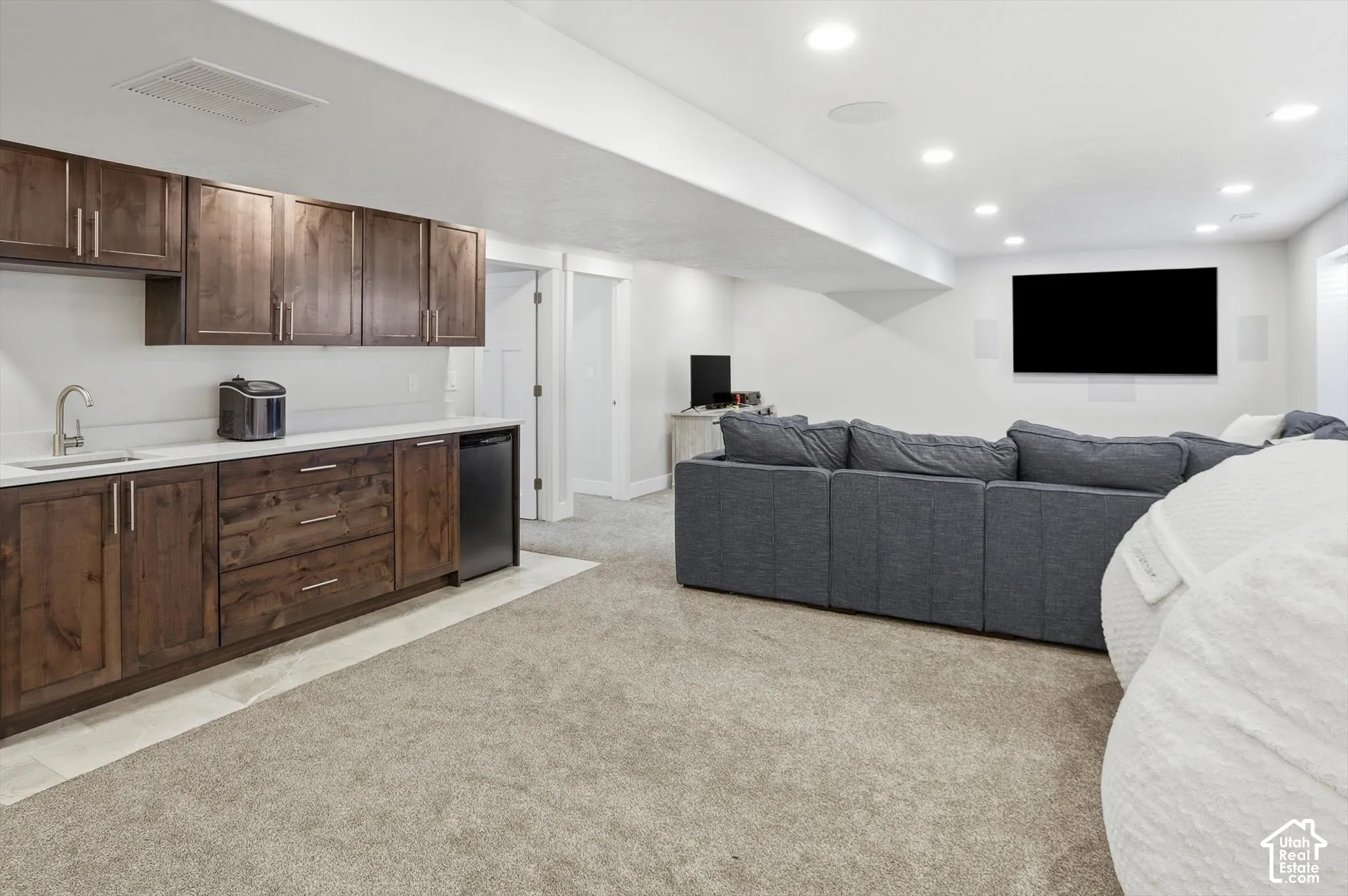 Wet bar featuring wood cabinetry, white countertops, a stainless steel sink, and a built-in beverage refrigerator, complemented by recessed lighting and carpeted flooring