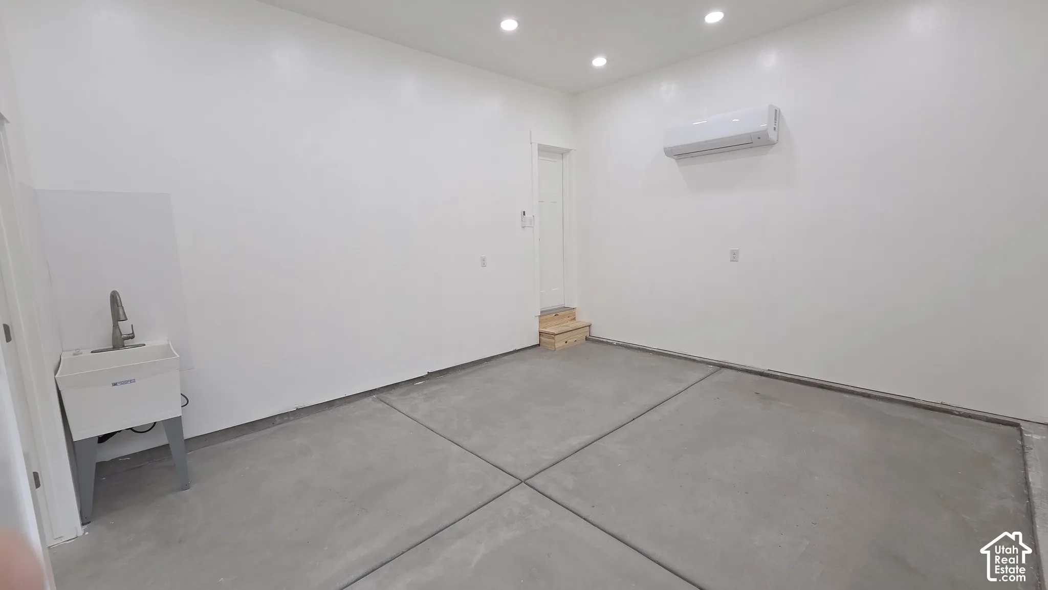 Finished garage space featuring recessed lighting, a wall-mounted climate control unit, concrete flooring, and a utility basin with a chrome faucet