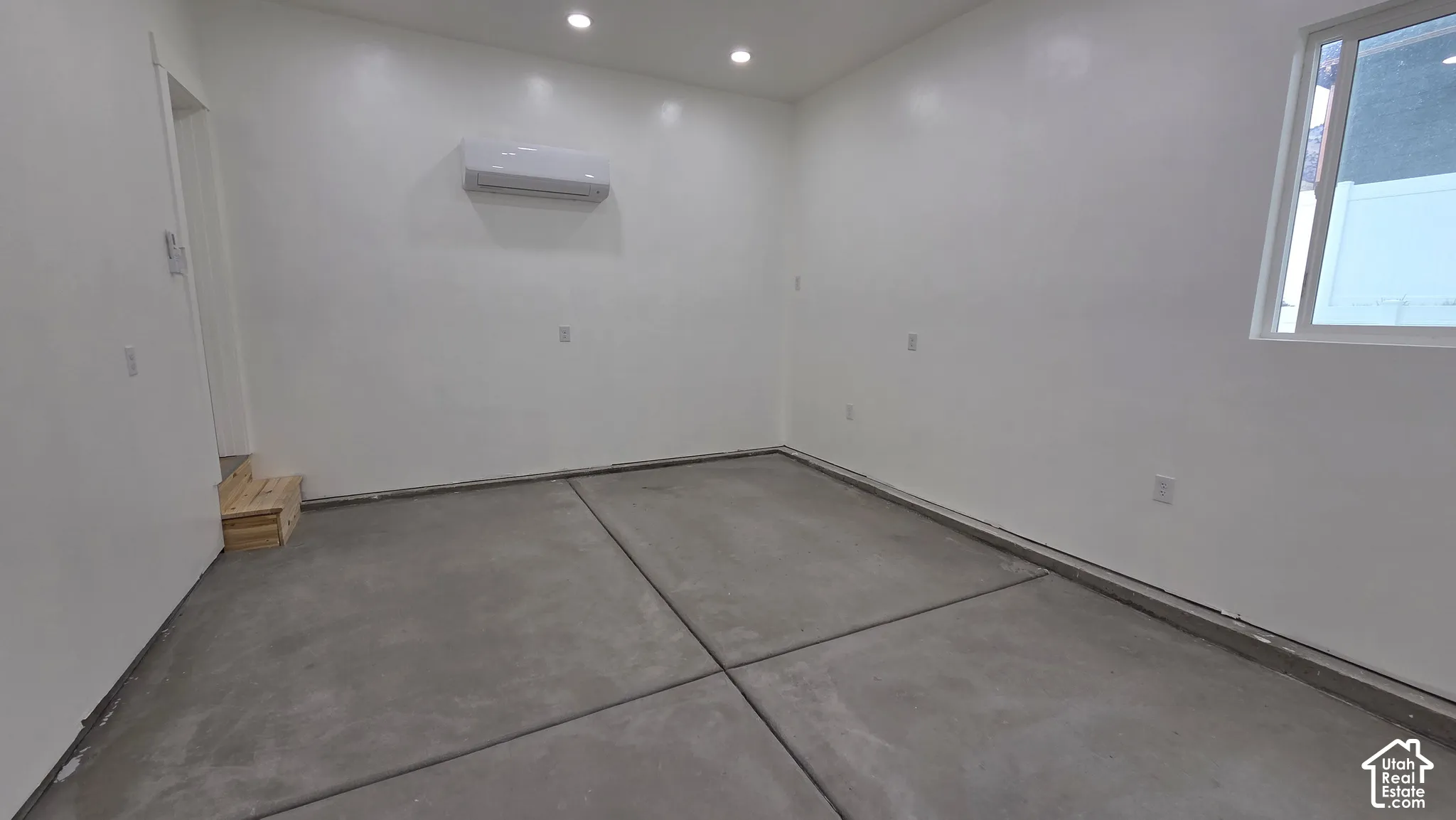 Interior space featuring smooth concrete flooring, recessed lighting, white walls, and a wall-mounted climate control unit