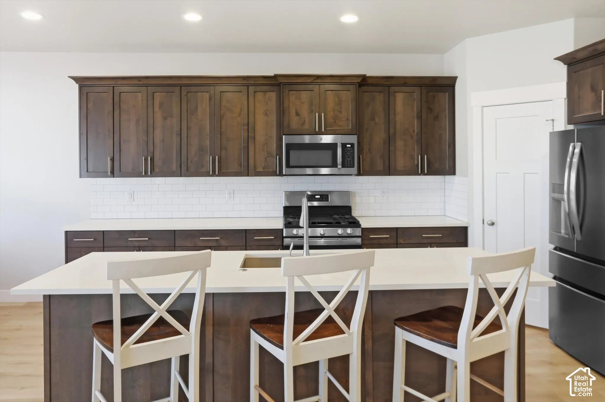 Kitchen featuring wood cabinetry, a central island with a solid surface countertop, white subway tile backsplash, and stainless steel appliances