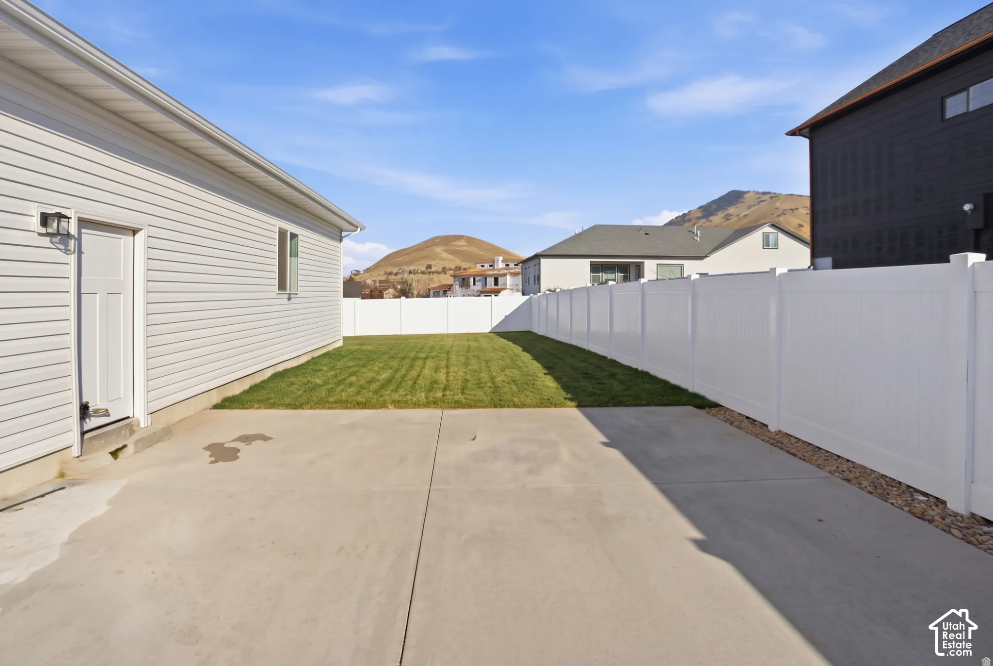 Concrete patio area with a fenced backyard, featuring horizontal siding, a white vinyl privacy fence, and mountain backdrop
