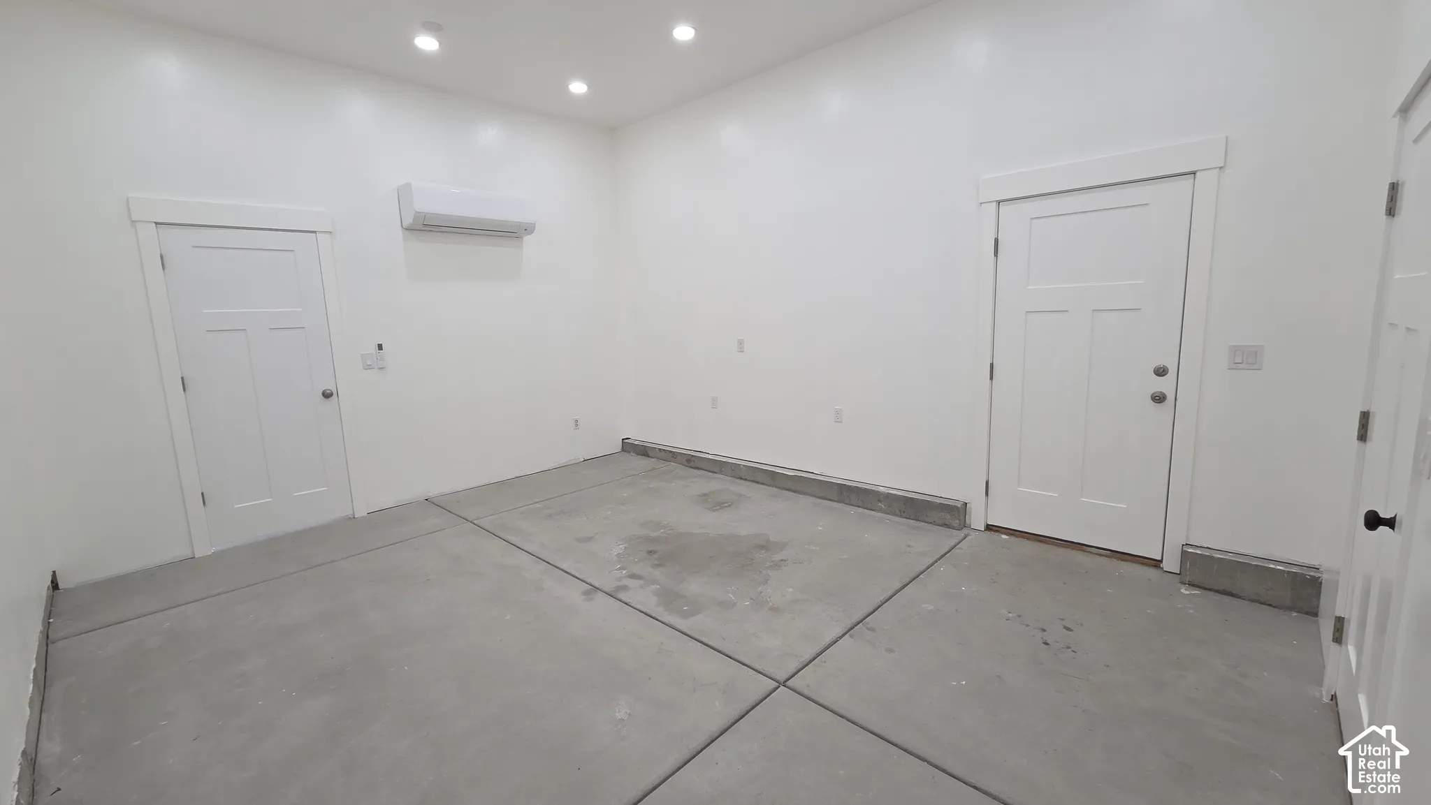 Interior space featuring concrete flooring, recessed lighting, wall-mounted climate control unit, and two-panel shaker-style doors