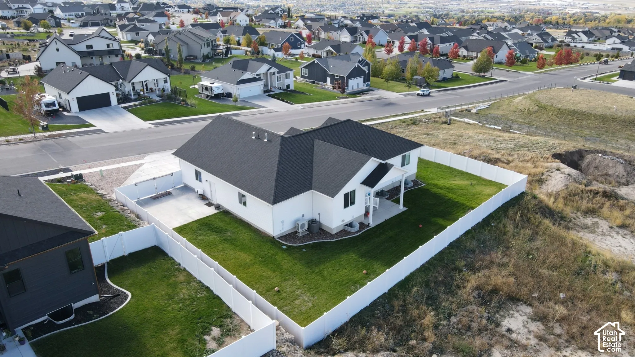 Single-story residence featuring a white exterior, dark asphalt shingle roof, concrete patio, and a fully enclosed vinyl privacy fence surrounding the rear lawn