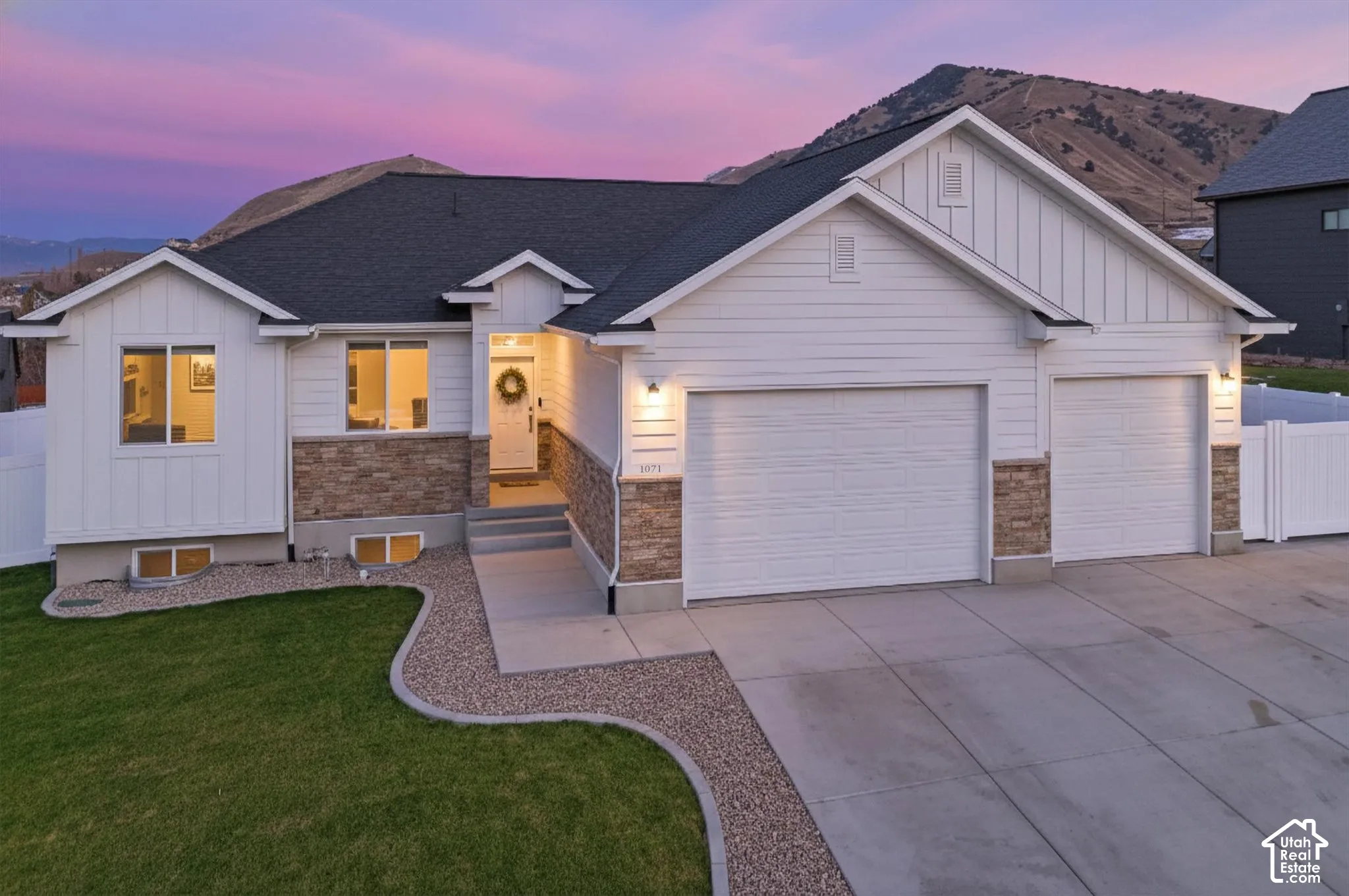 Single-level residence featuring a dual-tone exterior with stone veneer and white horizontal siding, an attached three-car garage, concrete driveway, and a mountain backdrop