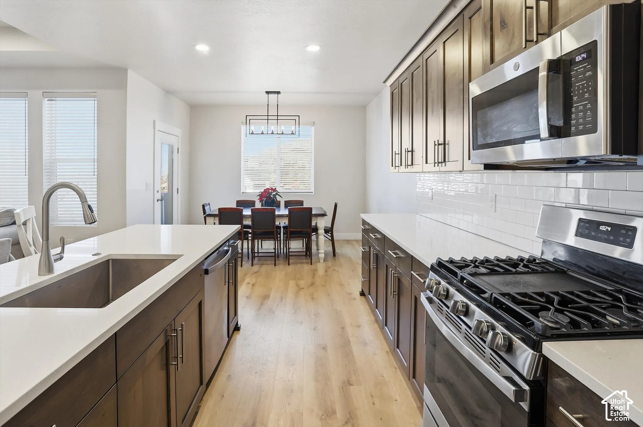 Kitchen featuring wood-finish cabinetry, quartz countertops, a white subway tile backsplash, stainless steel appliances, and wood-finish flooring