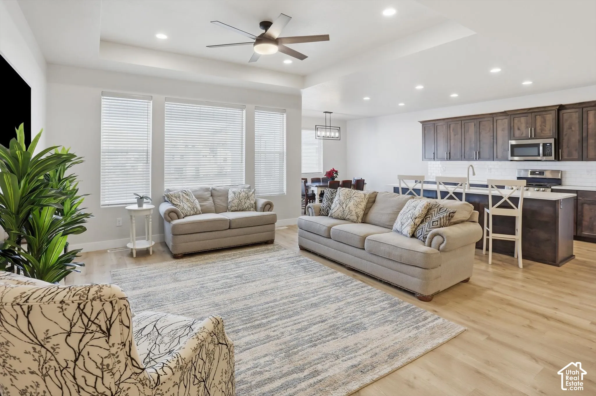 Open-concept interior featuring a tray ceiling, recessed lighting, wood-finish flooring, dark-toned cabinetry, and a kitchen island