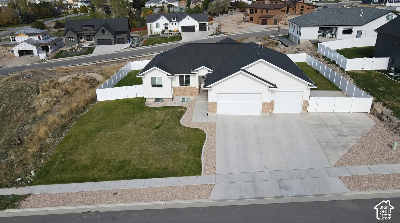 Single-level residence featuring a multi-gabled asphalt shingle roof, stone and stucco exterior, attached three-car garage, concrete driveway, and white vinyl perimeter fencing
