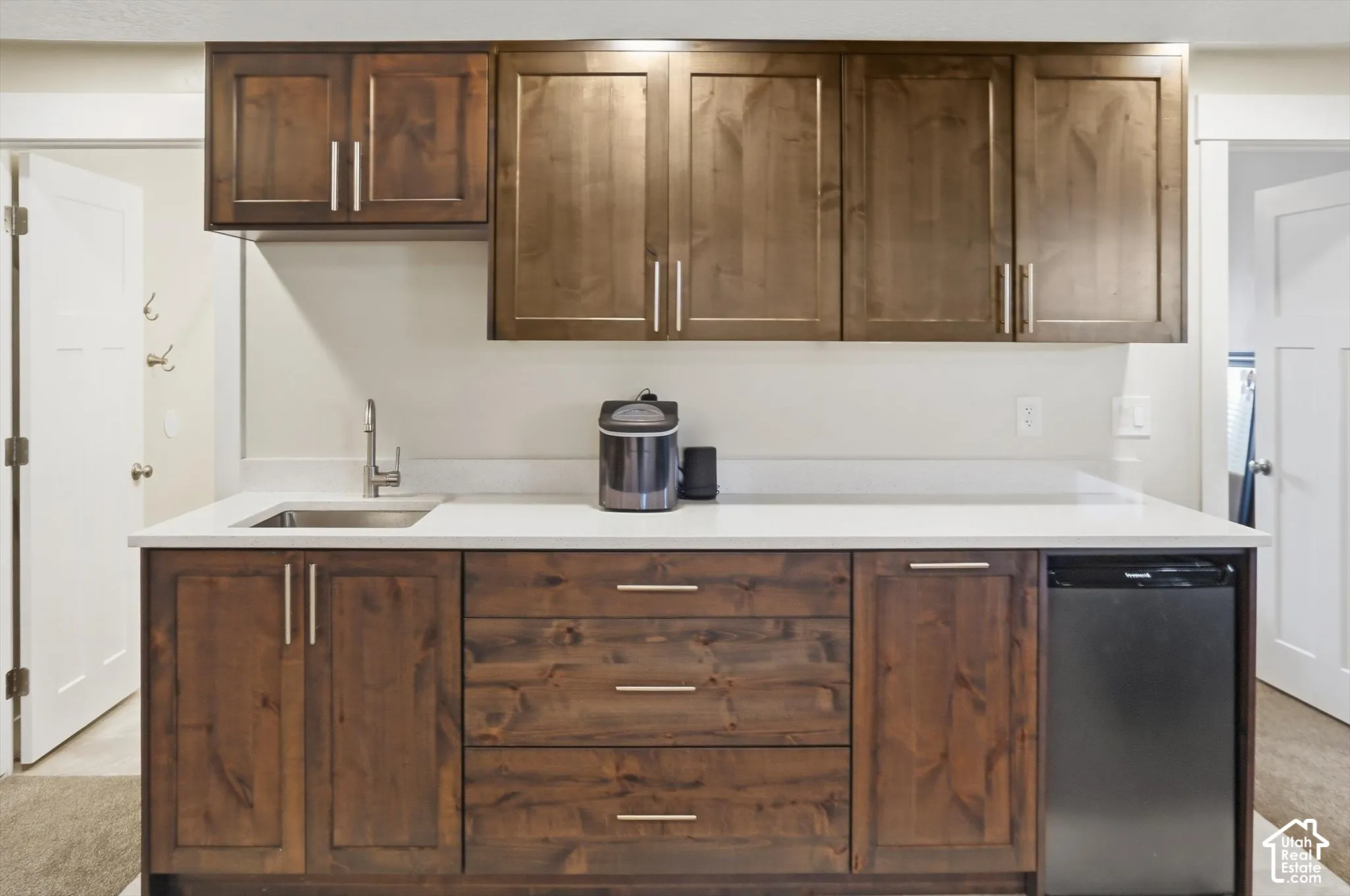 Kitchenette featuring stained wood cabinetry, stone-finish countertops, stainless steel undermount sink, and integrated under-counter refrigeration