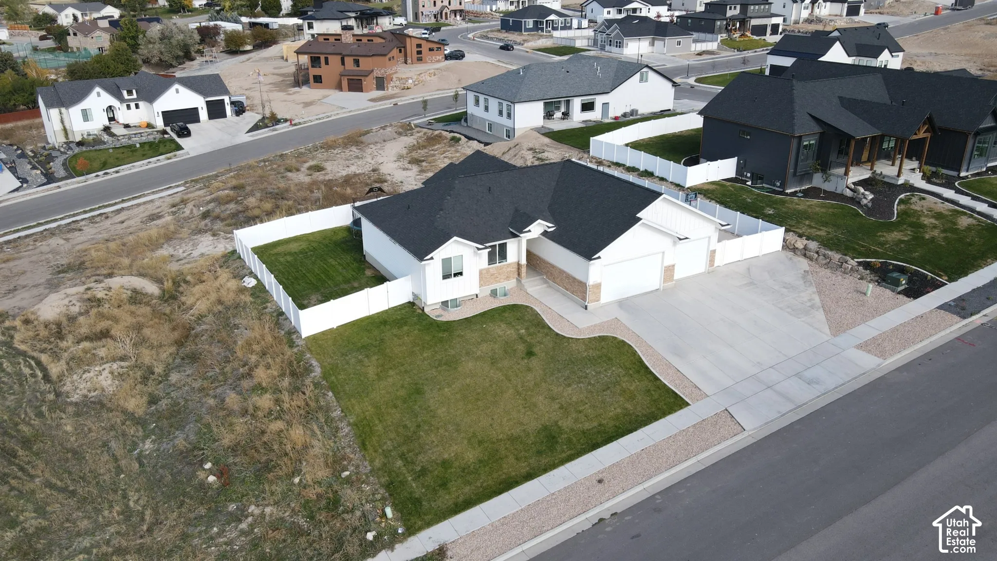 Single-story residence featuring a multi-gable roof, attached three-car garage, white vinyl fencing, and a concrete driveway