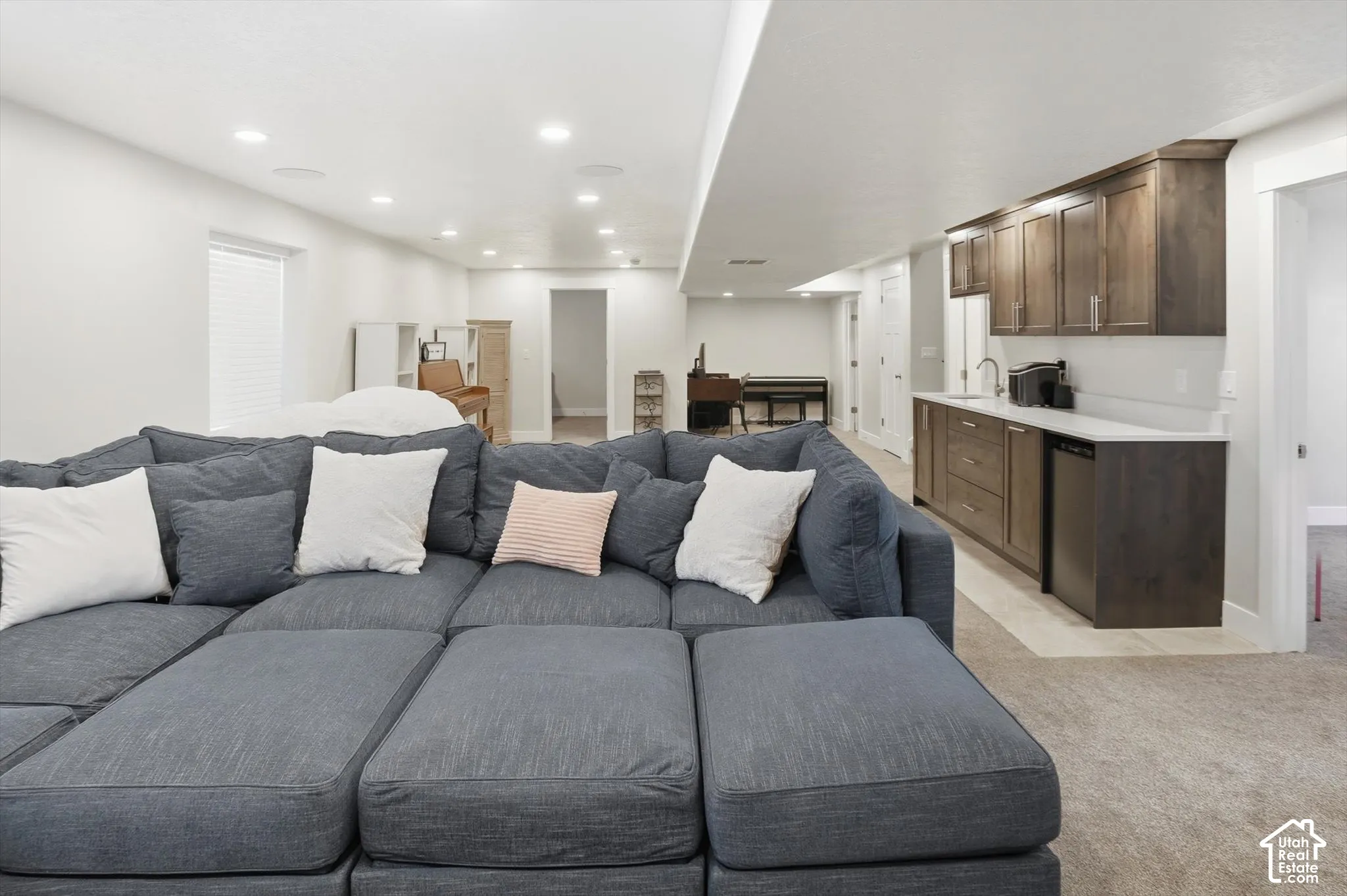 Finished space featuring recessed lighting, wet bar with dark-toned cabinetry, light-toned countertops, and neutral carpeting