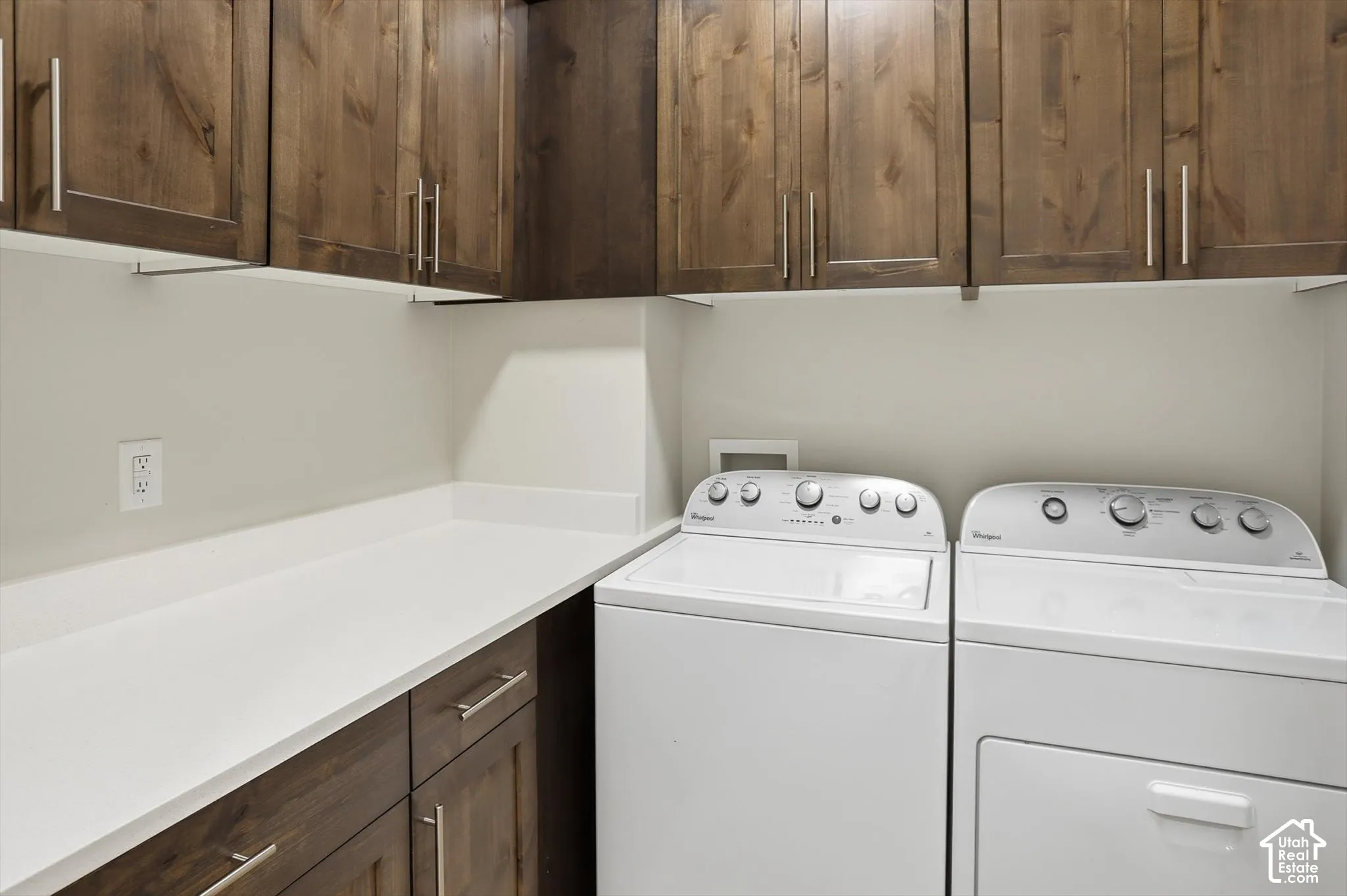 Laundry room featuring stained wood cabinetry, a solid-surface countertop, and stainless steel hardware