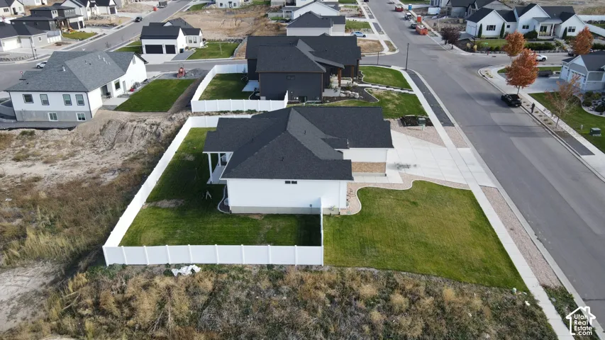 Aerial perspective featuring a white vinyl-fenced rear yard, multi-pitched shingle roof, concrete driveway, and a corner lot configuration