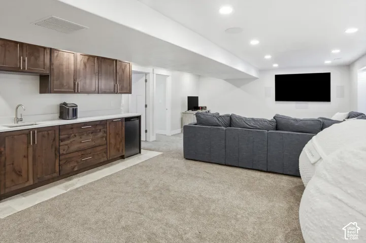 Wet bar featuring wood cabinetry, white countertops, a stainless steel sink, and a built-in beverage refrigerator, complemented by recessed lighting and carpeted flooring