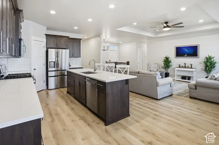 Kitchen featuring dark-stained cabinetry, quartz countertops, a central island with an undermount sink, recessed lighting, and wood-finish flooring