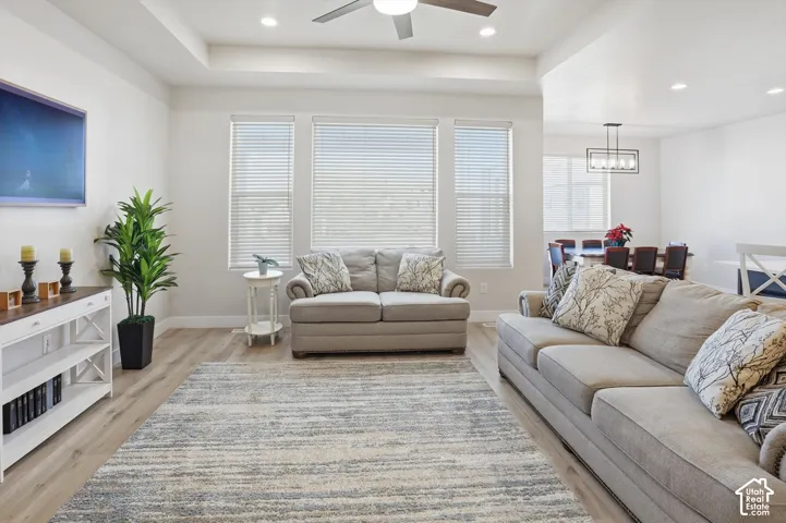 Living area featuring a tray ceiling, recessed lighting, wood-finish flooring, and triple windows with horizontal blinds